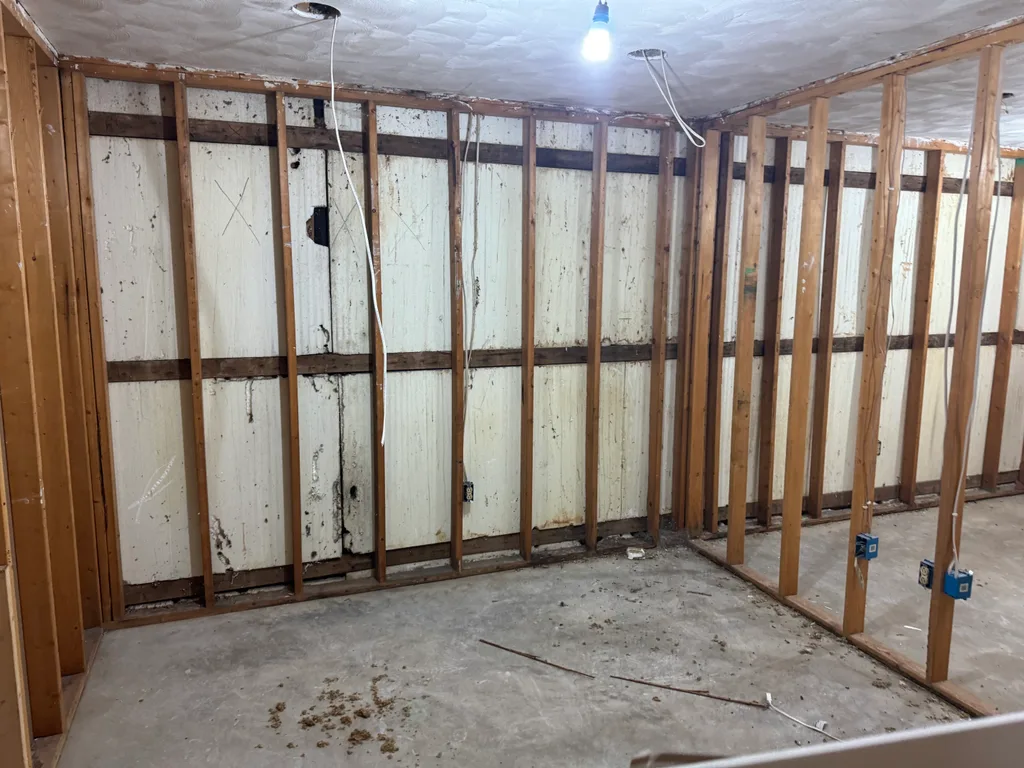 Empty framed room with bare studs, concrete floor and a single hanging bulb