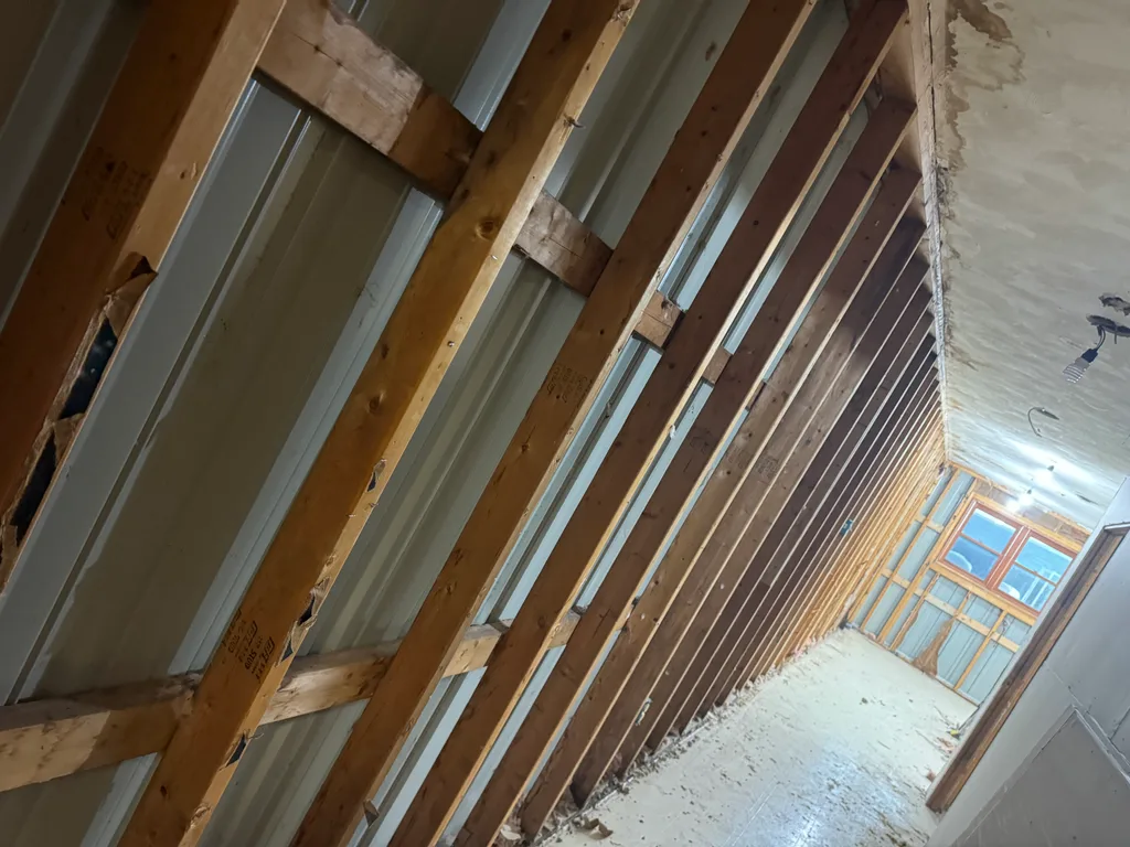 Sloped attic space with dark timber rafters, steel roof panels and a window at the far end