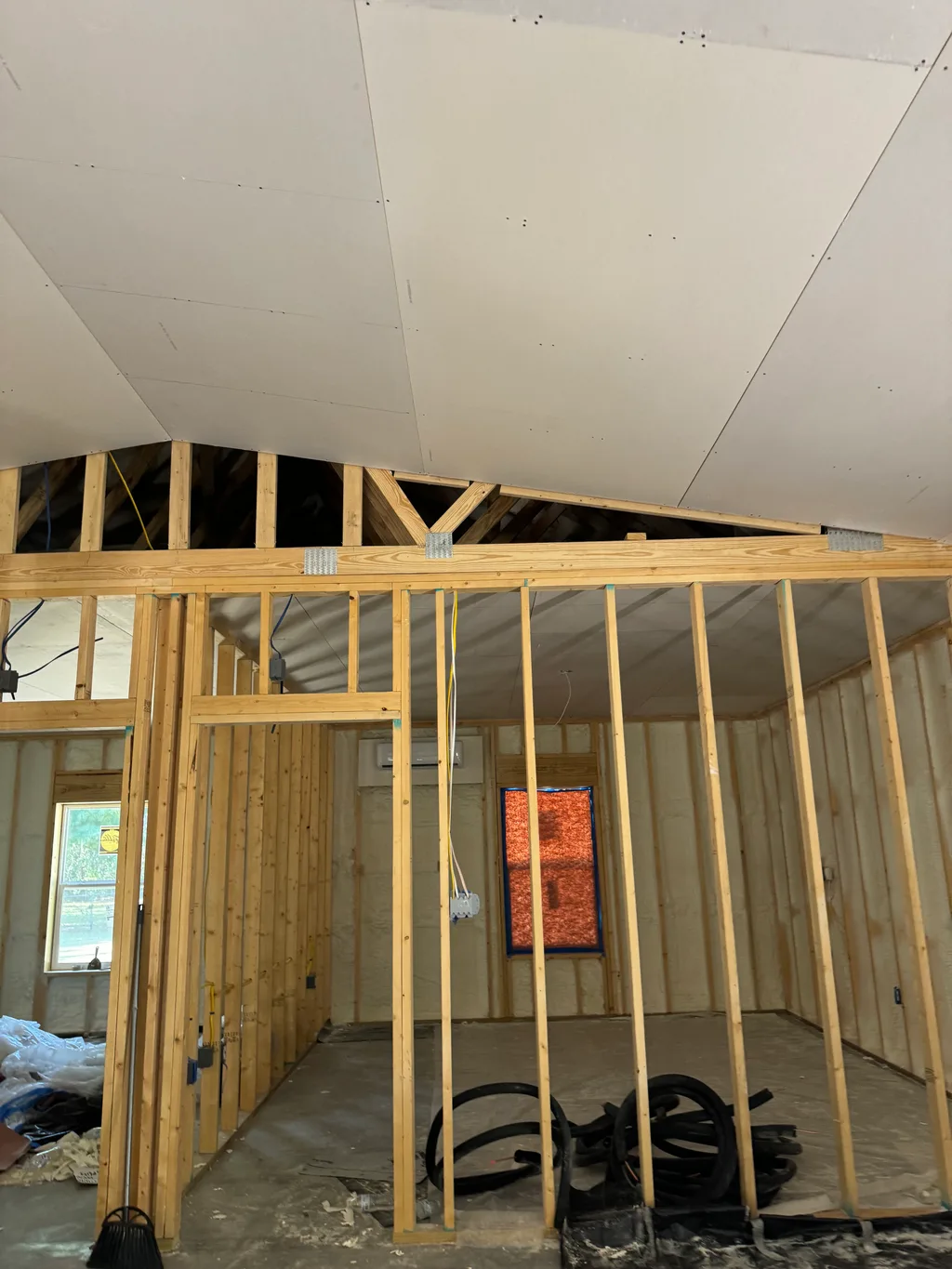 Framed loft under a drywall ceiling with an orange grille and coiled hoses below