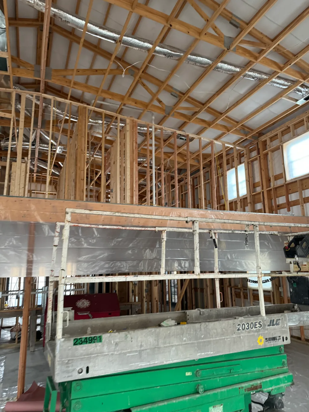 Green scissor lift and plastic sheeting inside a barn part way through framing