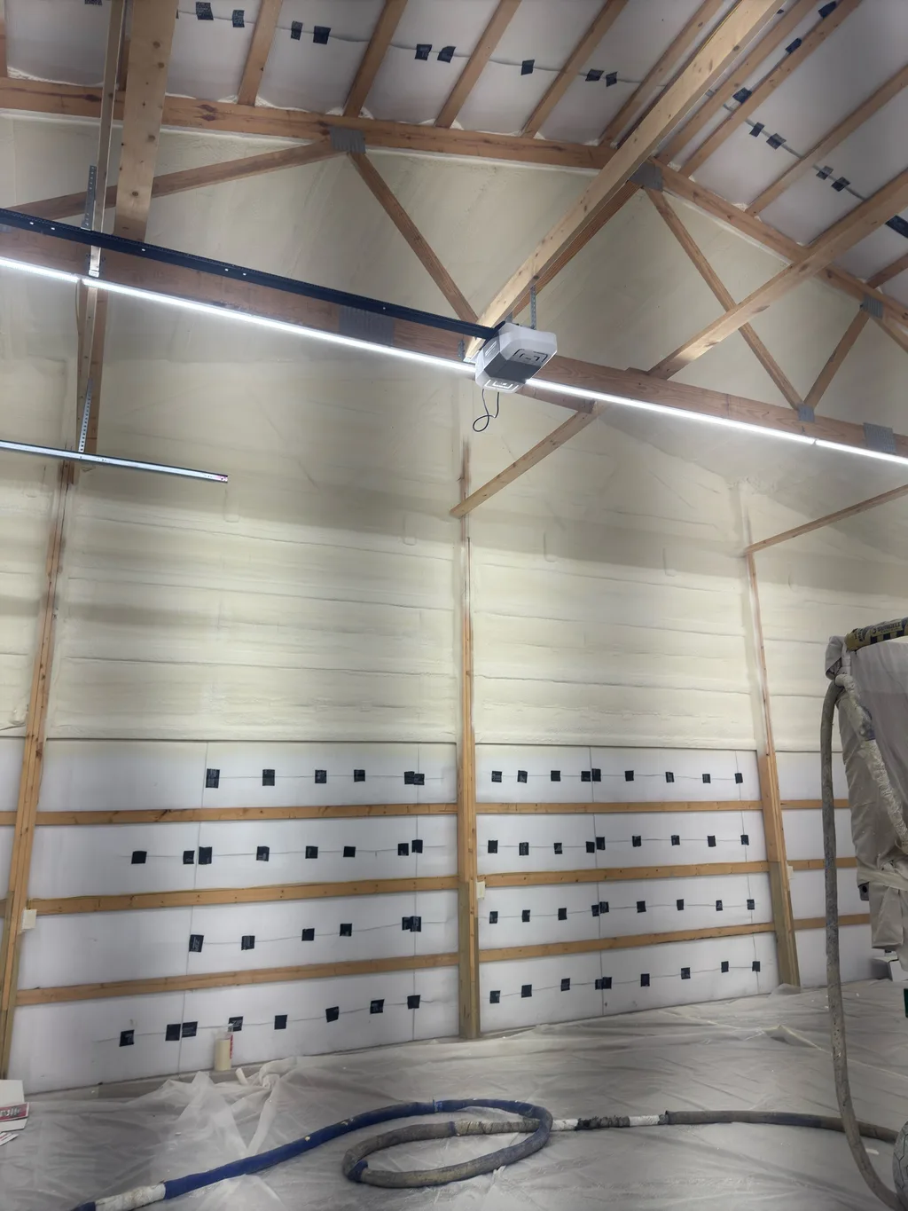 White lined barn interior with a blue spray hose coiled across the covered floor