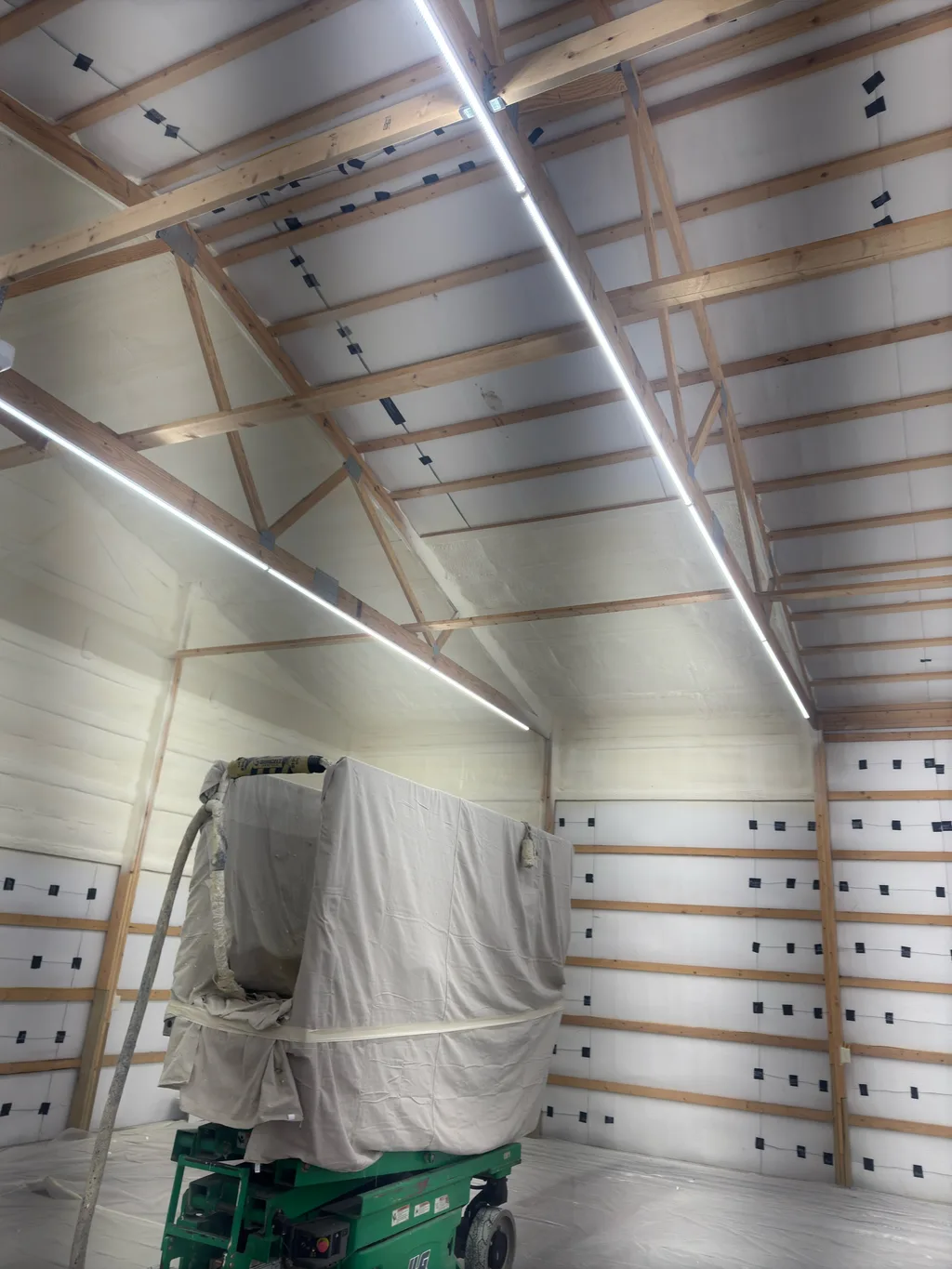 Green scissor lift carrying a covered machine inside a barn lined in white sheeting