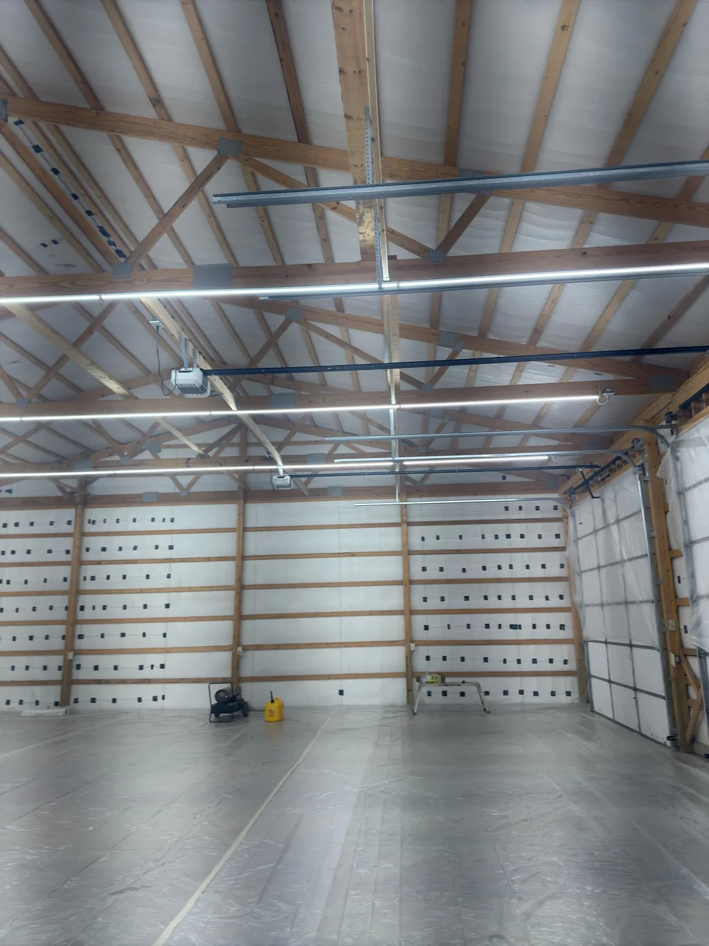 Empty barn bay lined in white with strip lights running along the timber purlins