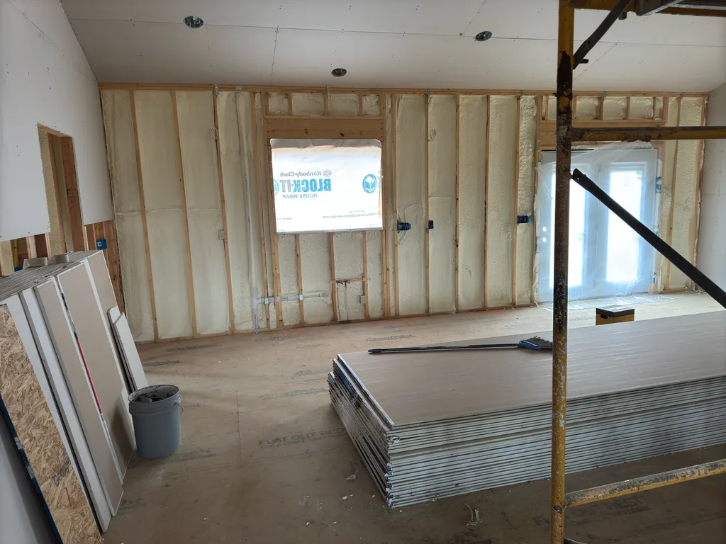 Foamed wall of a new room with drywall sheets stacked and scaffolding to one side