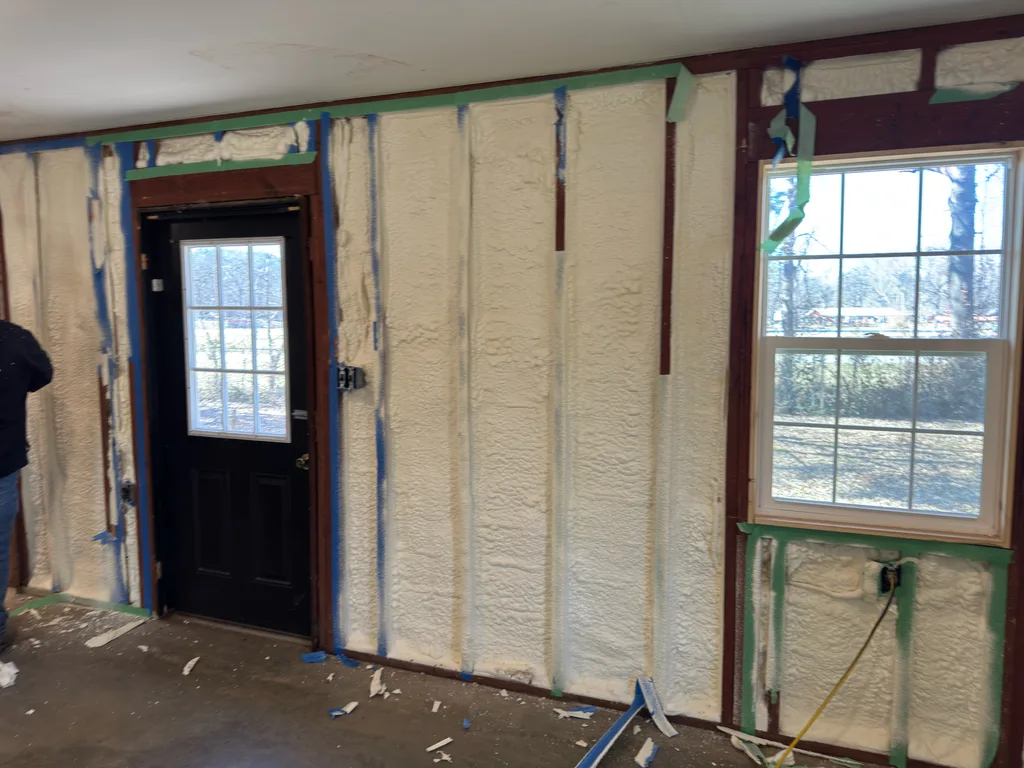 Foamed wall around a black entry door and window with blue and green masking in place