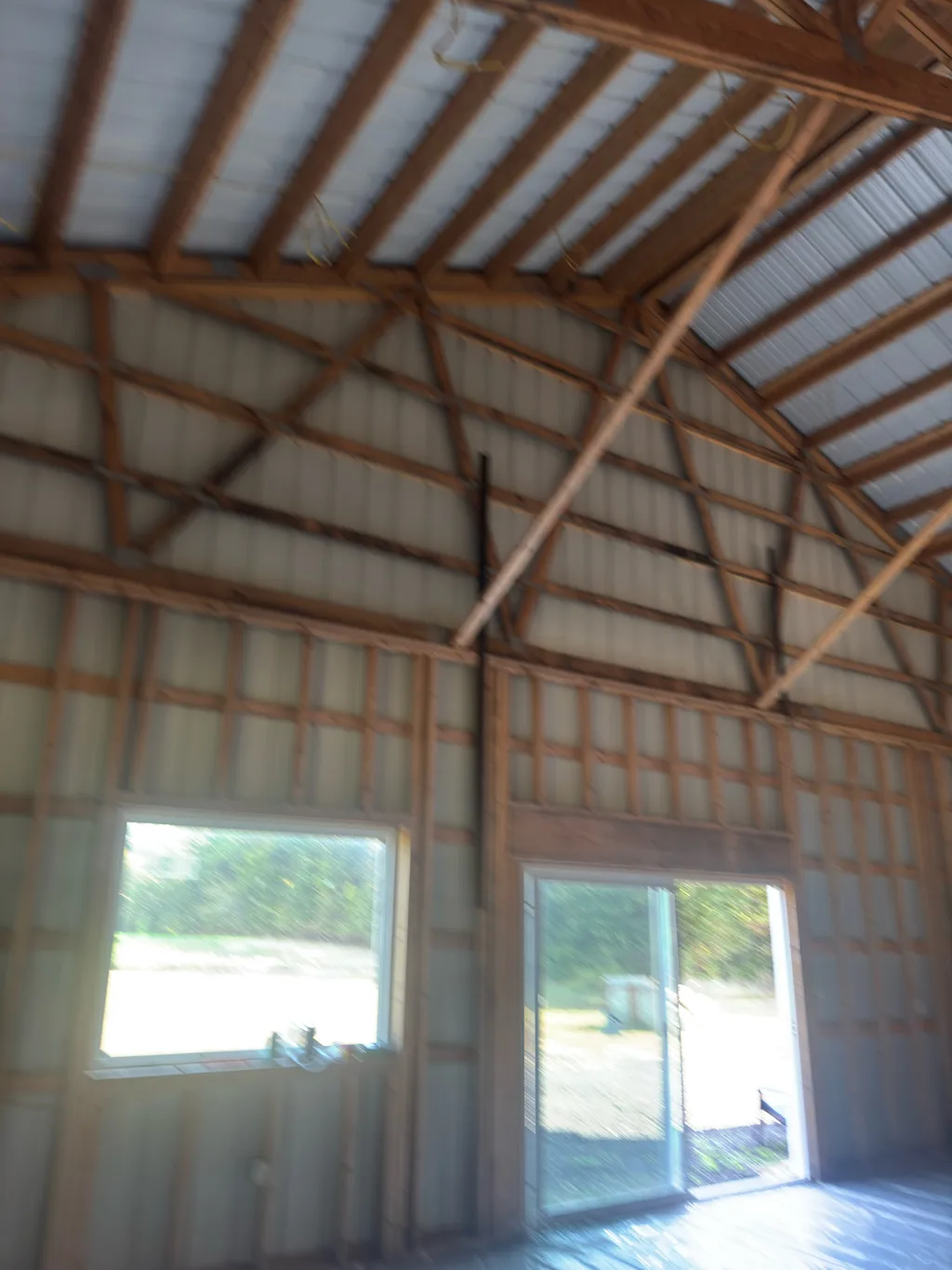 Timber framing under a steel roof with daylight through two windows on the far wall