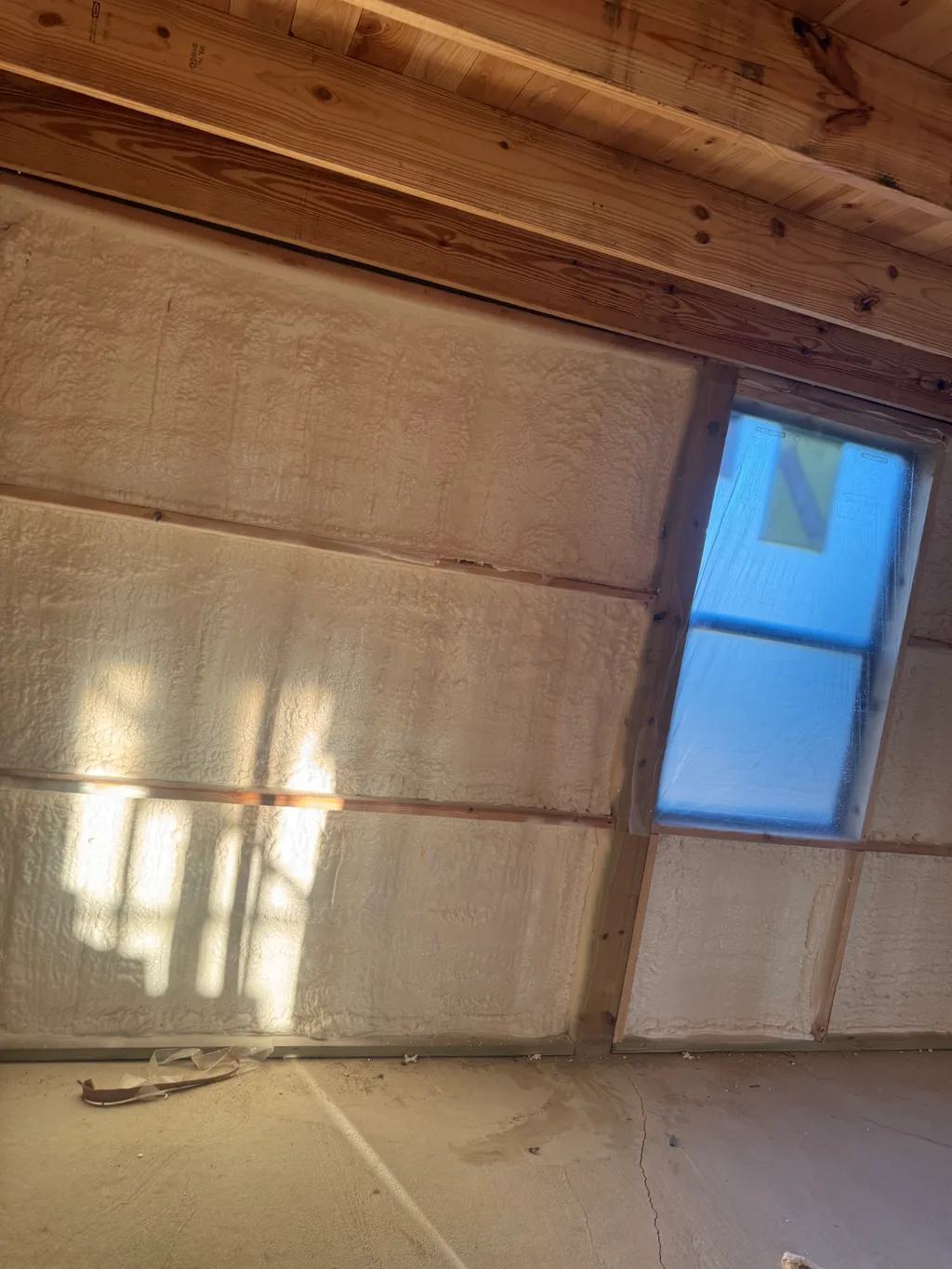Sunlight falling across a foamed wall beside a small window in a timber framed room