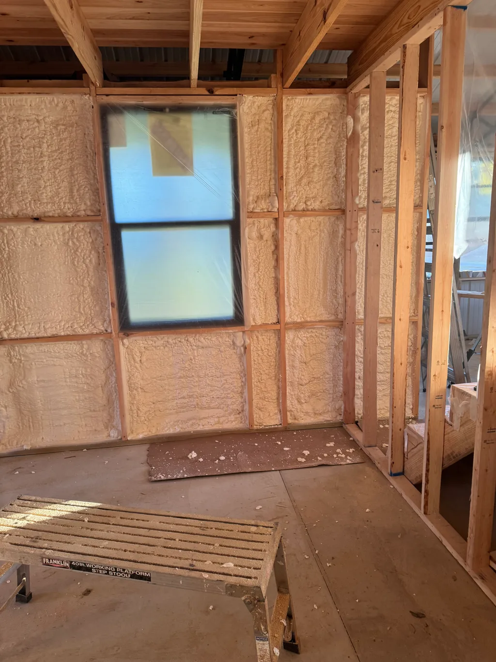 Foamed wall and window with open timber framing and a sawhorse on the floor